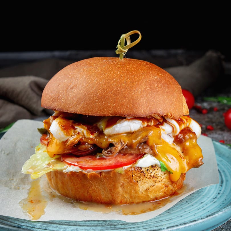 A large burger with melted cheese, white sauce, lettuce, and tomato on a bun.