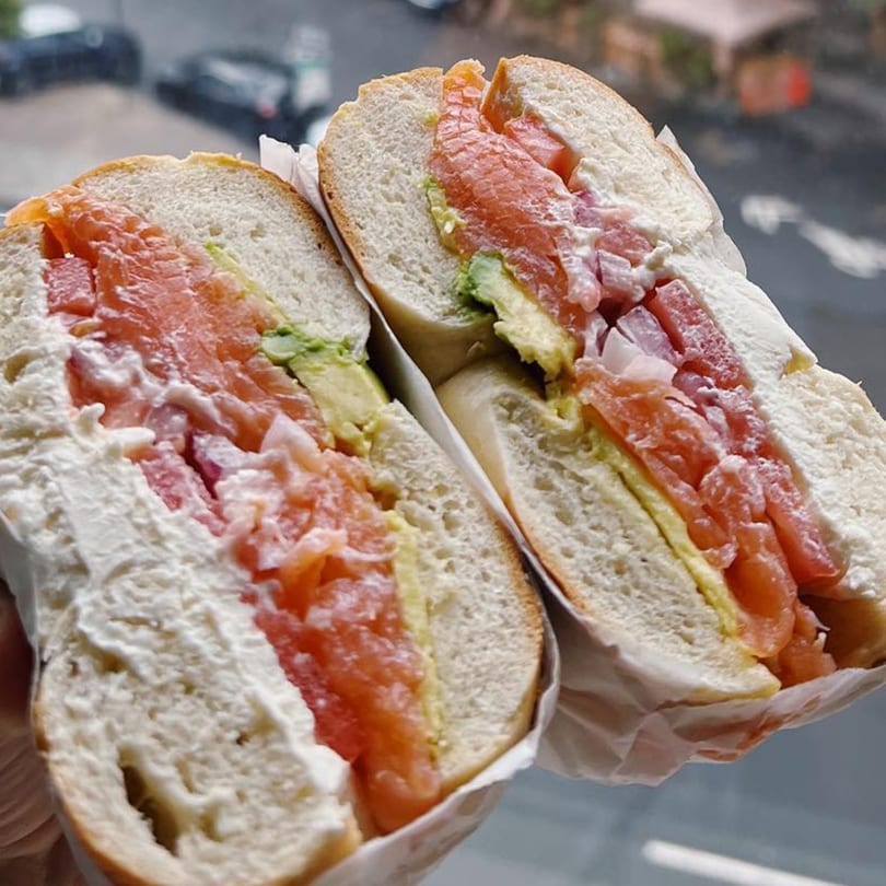 A Tribeca Bagels lox and cream cheese bagel with avocado and tomatoes, cut in half.
