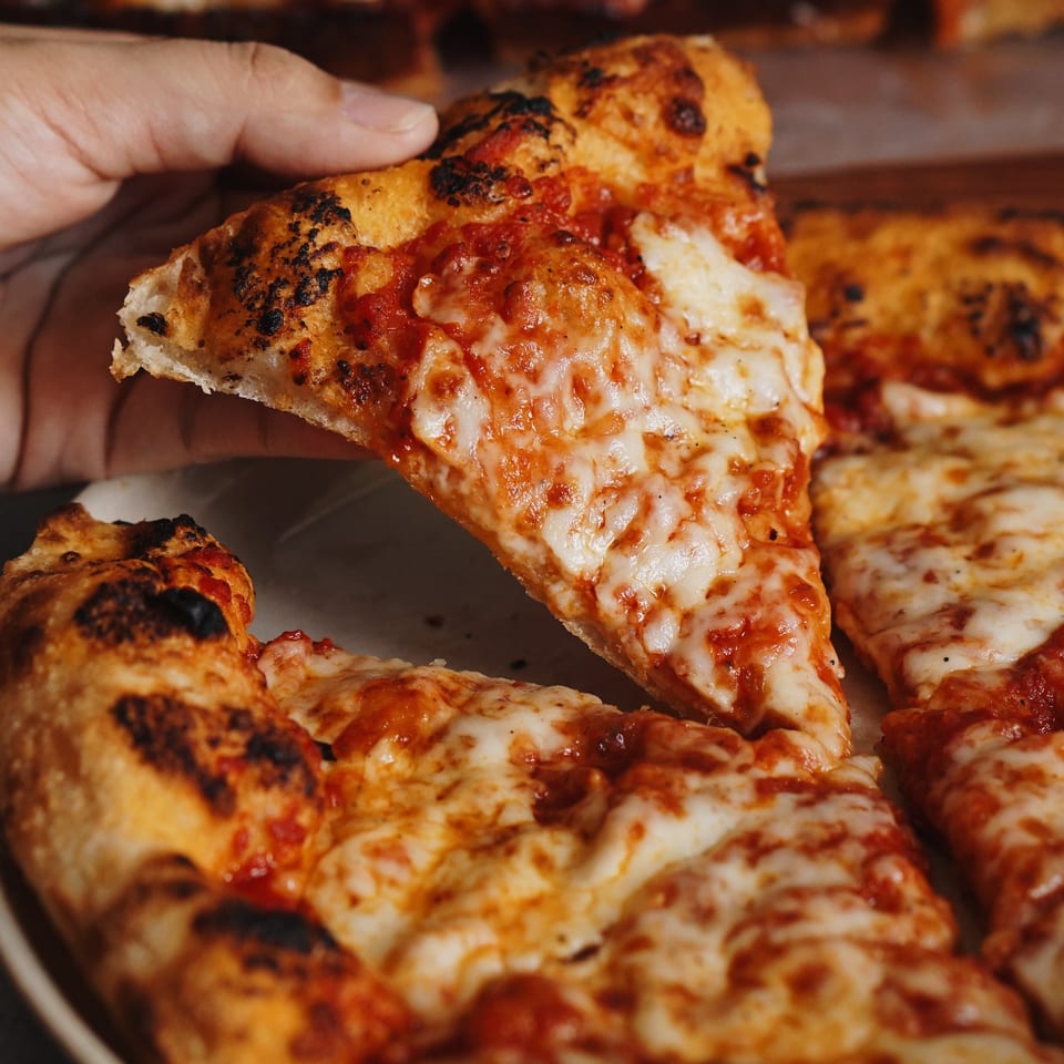 A hand lifts a slice of cheesy pizza with a crispy crust from a whole pizza.